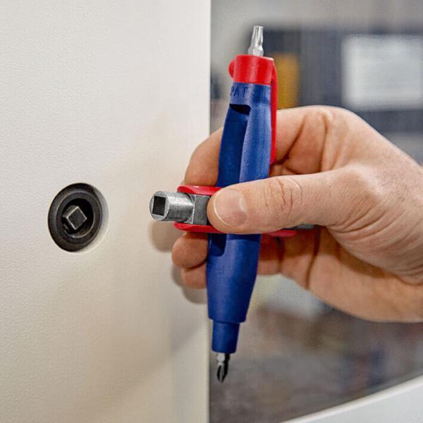 Ein Handwerker hält ein spezielles Werkzeug mit ergonomischem Griff. Es hat einen Schraubendreher und einen Aufsatz für eine Sechskantschraube, der auf ein Loch an einer weißen Oberfläche zeigt.