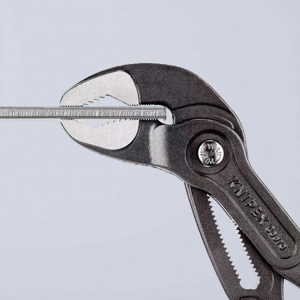 The image shows a pair of metal tongs with a diamond-shaped gripping surface. It is holding a narrow, straight object in the middle. The background is uniformly light.