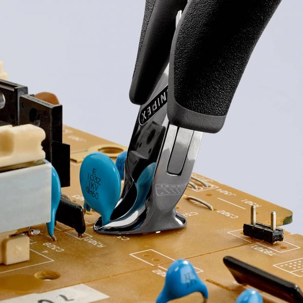 On a circuit board, blue electronic components are visible. A pair of pliers is gripping a component. The background is bright, and the pliers have black handles.