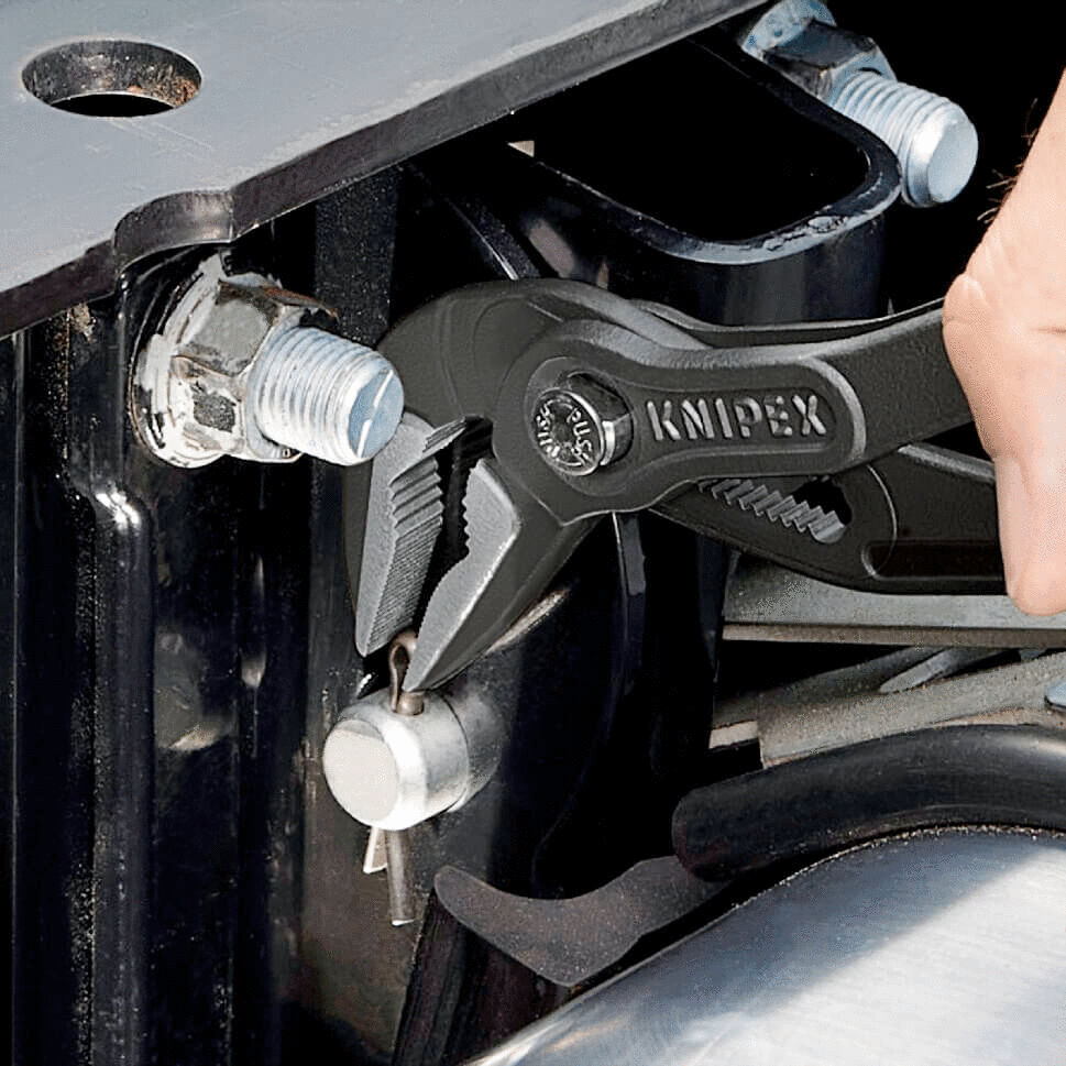 The image shows a hand holding a black Knipex plier, working on a screw on a metallic object. The background is industrial and metallic.