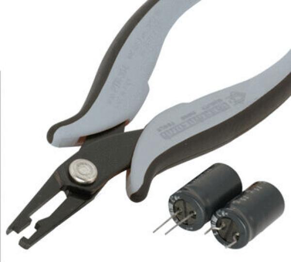 The image shows a special pair of pliers with flat, pointed jaws, ideal for electronic work. Next to the pliers, there are two black capacitors with two metal pins.