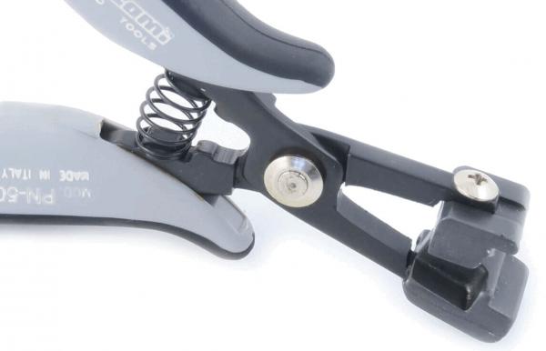 Das Bild zeigt eine graue, ergonomische Zange mit einer Feder. Die Zange hat eine schlichte, funktionale Form und eine schwarze Halterung mit einem Befestigungselement.
