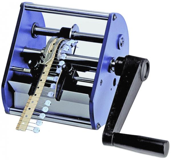 Das Bild zeigt eine manuelle Maschine mit einem großen, rechteckigen Gehäuse und einer Kurbel. An der Vorderseite führt ein flexibles Band durch die Maschine, die in der Mitte Drehmechanismen hat.