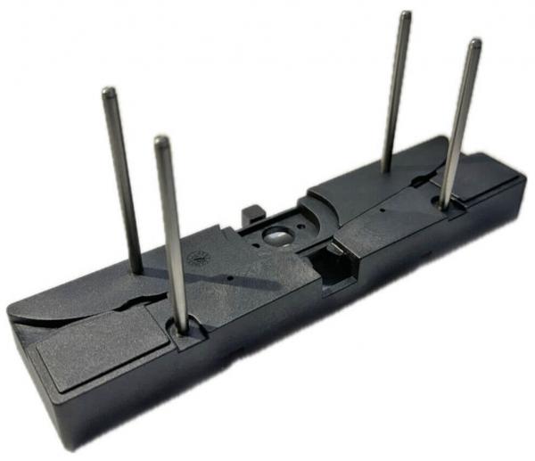 The image displays a black, rectangular component with two side arches. It features three metallic pins protruding vertically, as well as a central recess.
