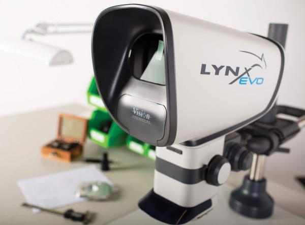 Das Bild zeigt ein Gerät namens LYNX Evo, das wie ein kleiner Telescop aussieht. Es hat eine schwarze Öffnung vorne, eine graue und weiße Hülle und steht auf einem stabilen grauen Sockel.