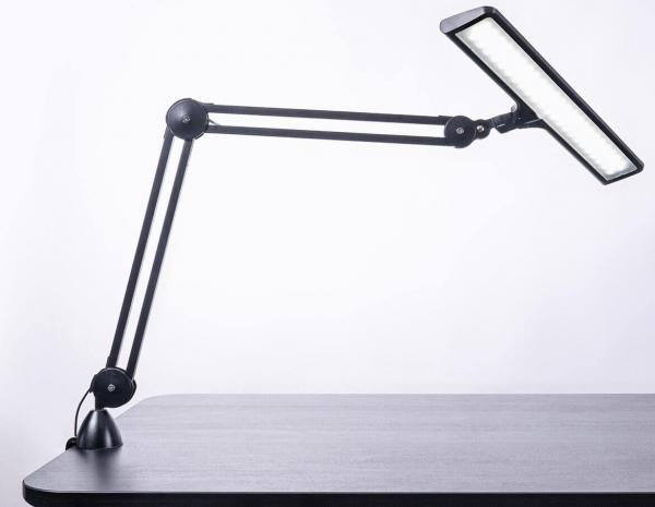 The image shows a black desk lamp with a flexible arm system. The lamp head is elongated and has a bright light source that is angled downwards.