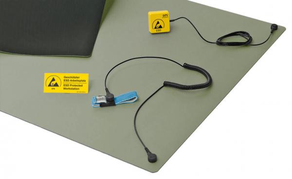 The image shows a green ESD work mat. Attached to the mat are a yellow safety symbol, a blue grounding clip, and a cable with a plug.