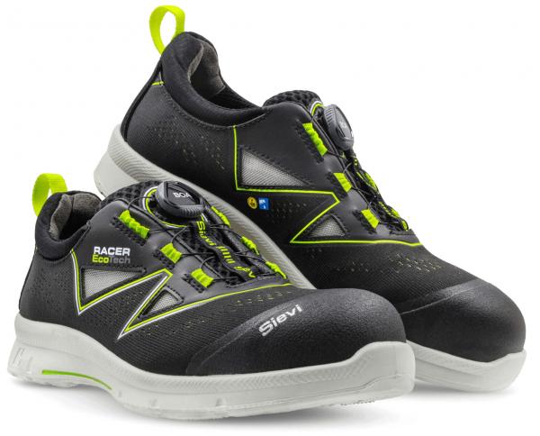 The image shows a pair of black work shoes with green accents. They feature a quick-lacing system and a sturdy, light-colored sole. The text "Racer Eco Tech" is visible.