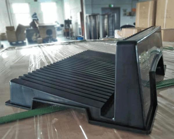 The image shows a black, rectangular object with a wavy surface and vertical grooves. It appears to be standing on a transparent base, surrounded by blurry boxes.