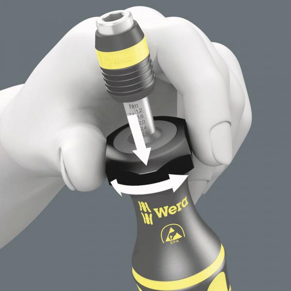 The image shows a hand holding a screwdriver. The screwdriver has a rubberized grip area with the inscription "Wera". At the top is a torque scale with arrows that illustrate the function.