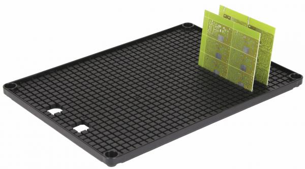 The image shows a rectangular, black plate with a grid pattern. On it is a green, thin piece with square fields, which is slightly tilted.