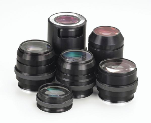 The image displays multiple black camera lenses in various sizes and shapes. Some lenses feature a shiny, transparent surface, while others are matte. They are artfully arranged.