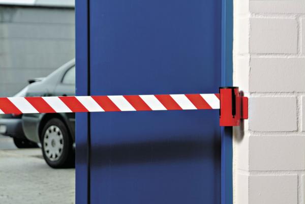 The image shows a blue door secured with a red-and-white barrier. In the background, a gray car is parked in front of the door. The adjacent wall is white.