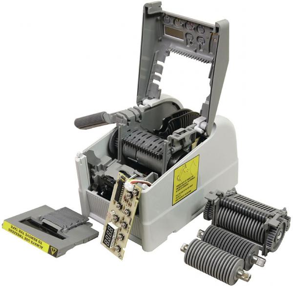 The image shows an open mechanical device with a gray casing. Inside, gears and a circuit board are visible. On the side, there is a small black block, presumably a part of the device.