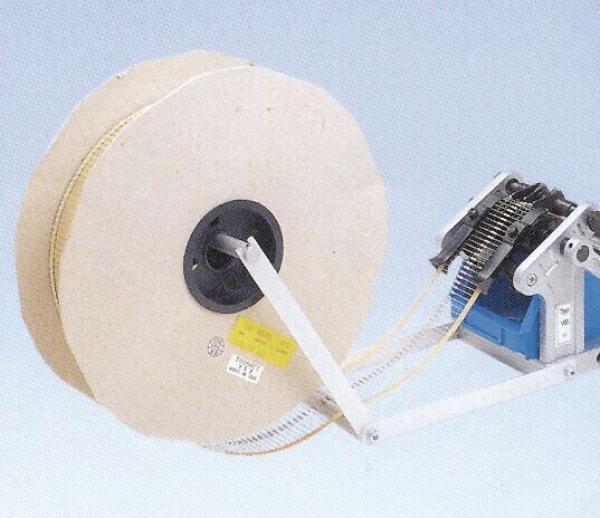 Das Bild zeigt eine große, runde Rolle aus hellem Material, an der eine Mechanik mit einem Motor befestigt ist. Ein Riemen verbindet die Rolle mit der Mechanik.