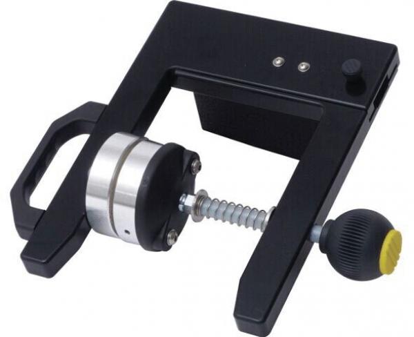 The image displays a black device with a textured grip and a round push element. It features an adjustment screw and a spring mechanism that ensures precision.