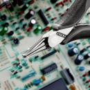 Preview: The image shows a pair of pliers holding a small electronic component, while in the background a complex circuit board with colorful components is visible.