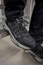 Preview: The image shows a black athletic shoe with a breathable upper and a thick, grippy sole. It is positioned on a metal step, surrounded by a neutral background.