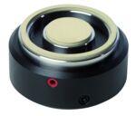 Preview: The image shows a round, black component with a central, flat element made of lightweight material. It has a red and a black connector on the side. This component could be part of a speaker or similar device.