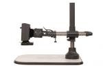 Preview: The image shows an optical device on a stable, rectangular table. It has a gray base, a vertical support, and an arm structure with a holder for lens-like objects.