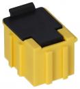 Preview: The image displays a small plastic plug. It has a bright yellow color with a black top. The sides are ribbed, and the shape is rectangular with a slightly rounded upper edge.
