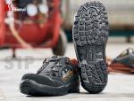 Preview: Das Bild zeigt ein Paar Sicherheitsschuhe mit einer robusten, profilierten Sohlenunterseite. Die Schuhe sind schwarz mit orangefarbenen Akzenten und einem praktischen Verschlusssystem.