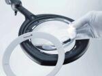 Preview: The image shows a magnifying glass with a round, clear lens. This is mounted on a black holder, while a hand wearing a white glove lifts the lens.