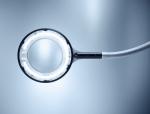 Preview: The image shows a large magnifying glass with a round, illuminated frame. It has a long, flexible neck and is positioned in soft light. The background is bright and monochromatic.