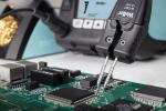 Preview: The image shows a circuit board with several black and silver chips. A tool that looks like a pair of pliers is holding one of the chips. In the background, you can see a soldering iron device.