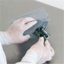 Preview: A person in white gloves is holding a green circuit board while removing it from a gray, shock-resistant packaging. The background is plain and neutral.