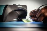 Preview: A device called Weller ShieldPro is placed on a blue background. A hand is holding a card while a tool is moved over it. The light from the device shines on the card.