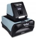 Preview: The image shows a device in black and light blue that looks like a small machine. On top, there is a vertical unit with buttons, and below, an area for inserting materials.