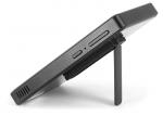 Preview: The image shows a thin, black device that is sleek and flat. It stands on a small, fold-out stand. Buttons are visible on the side.