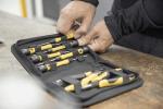 Preview: In the picture, you see hands rummaging through a toolbox with yellow and black tools. The box is placed on a table and contains various screwdrivers and pliers.
