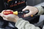 Preview: A hand holds a screwdriver with a red and yellow handle. Another small attachment is pushed onto the end. Tools are visible in the background.