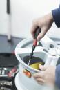 Preview: A hand holds a screwdriver tightening a screw on a silver rim. In the background, tools and a bright environment are faintly visible.