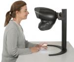 Preview: A woman is sitting at a table and looking at a device that looks like a magnifying device. She is holding a small, handy object in her hand.
