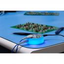 Preview: On a blue table lies a glowing, round adapter with cables. In the background, two green circuit boards are visible, equipped with various electronic components.