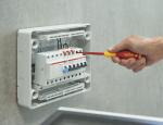 Preview: Ein Handwerker arbeitet an einem elektrischen Verteilerkasten an einer Wand. Er hält einen roten Schraubendreher und schraubt an Komponenten im Kasten, der beleuchtet und modern wirkt.